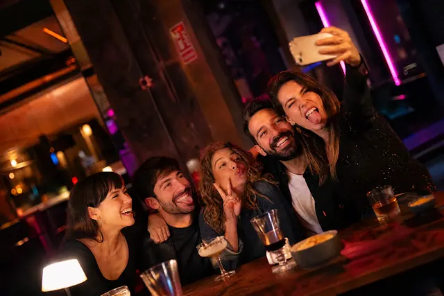 Fünf Freunde machen an einem Bartisch ein Selfie und ziehen Grimassen
